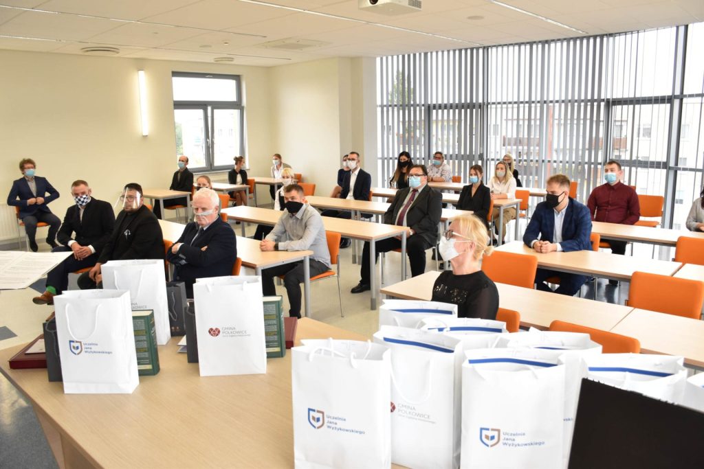 Uczestnicy uroczystości nagród siedzą przy oddzielnych stolikach; na pierwszym planie torby z logo UJW.