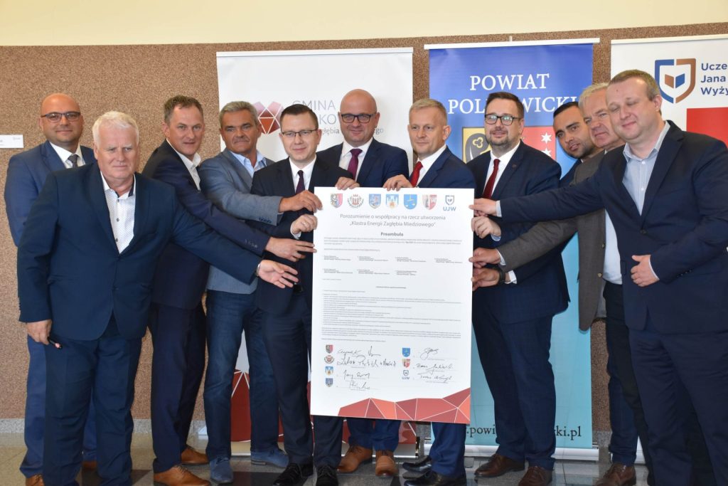 Przedstawiciele partnerów klastra energetycznego pozują z dużym dokumentem porozumienia.
