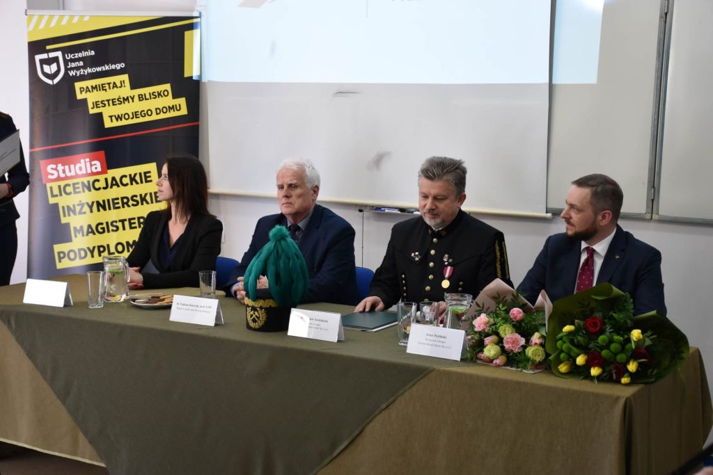 Kobieta i trzej mężczyźni siedzą przy stole z kwiatami i czakiem górniczym z zielonym pióropuszem.