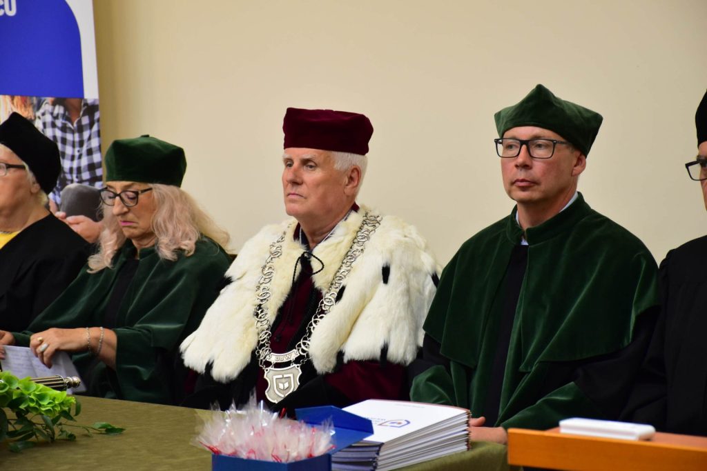 Przedstawiciele władz uczelni w strojach akademickich siedzą przy stole podczas uroczystości.