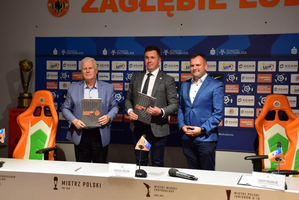 Trzej mężczyźni pozują przy stole konferencyjnym Zagłębia Lubin; dwaj prezentują dokumenty.