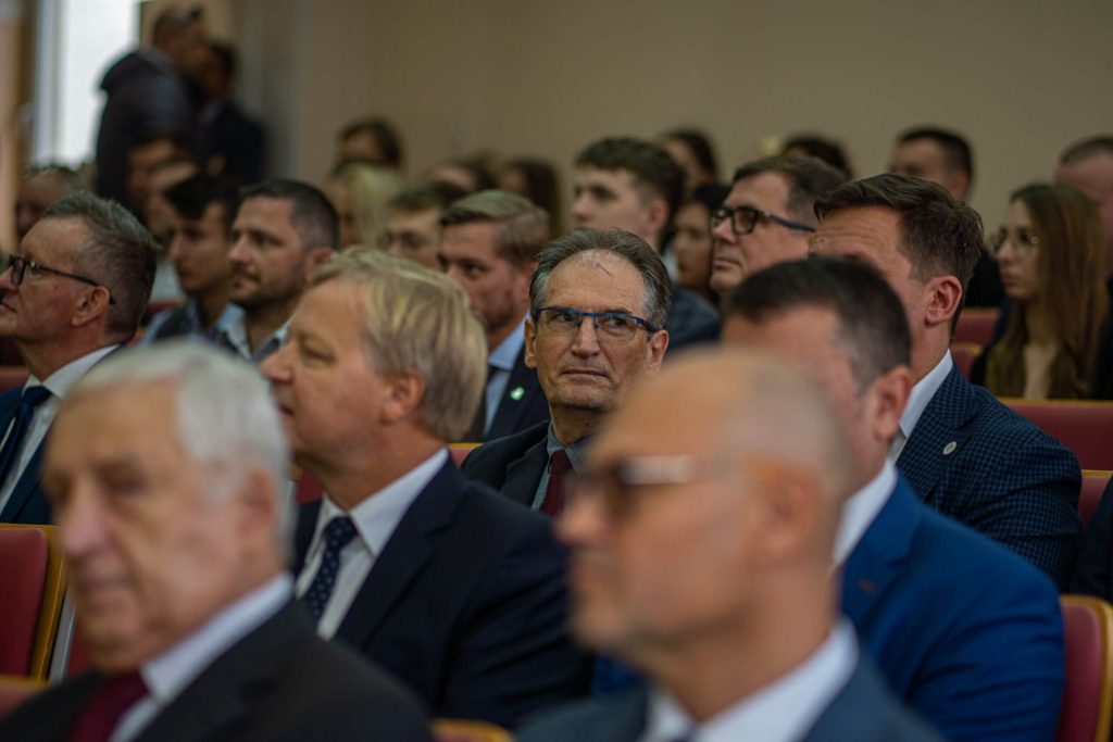 Uczestnicy inauguracji roku akademickiego siedzą w rzędach foteli w auli.