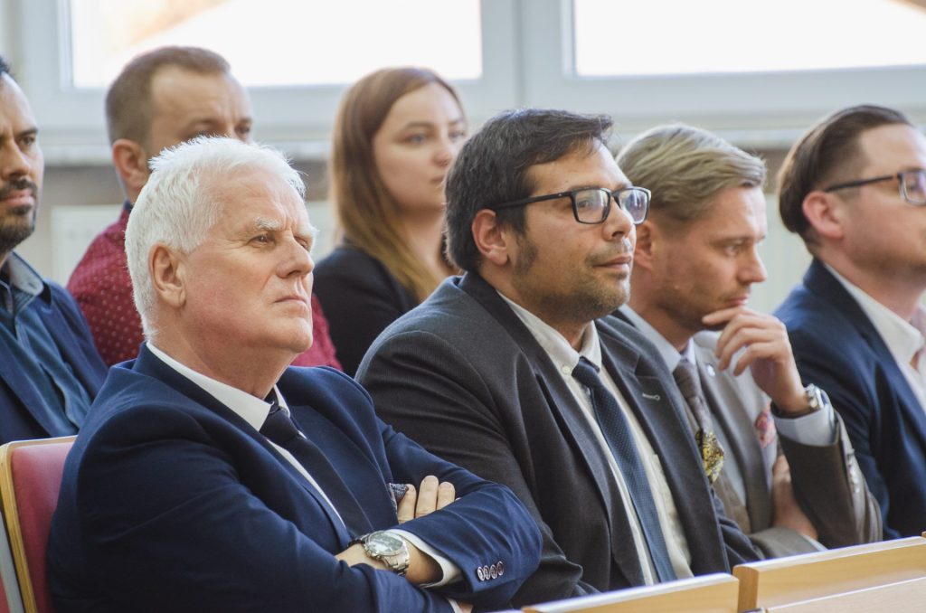 Mężczyźni w garniturach siedzą wśród publiczności uroczystości wręczenia nagród.