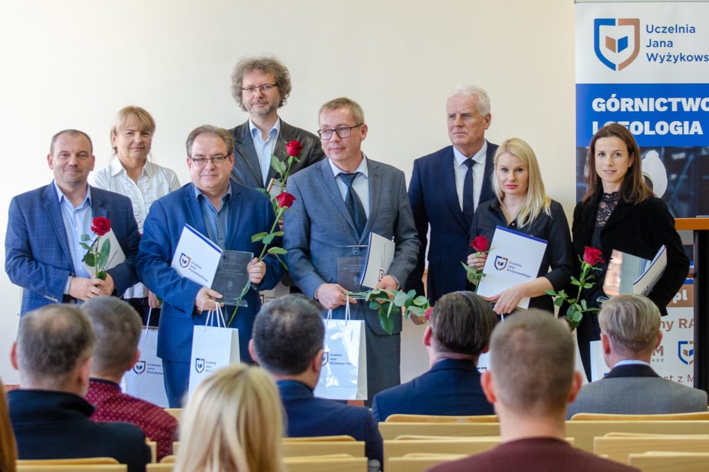Wyróżnione osoby prezentują certyfikaty, upominki i czerwone róże przed publicznością.