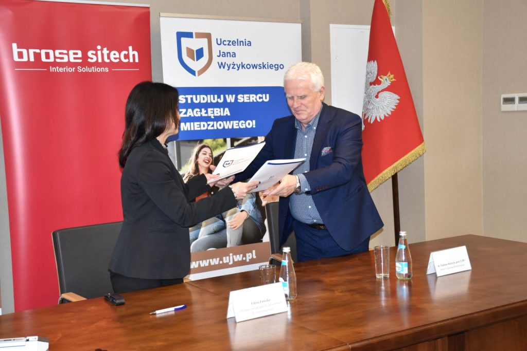kobieta i mężczyzna stoją przodem do siebie i przekazują sobie teczki z podpisaną przed chwilą umową