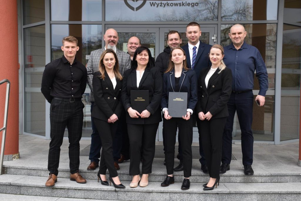 Grupa absolwentów i uczestników uroczystości pozuje na schodach przed wejściem do UJW.