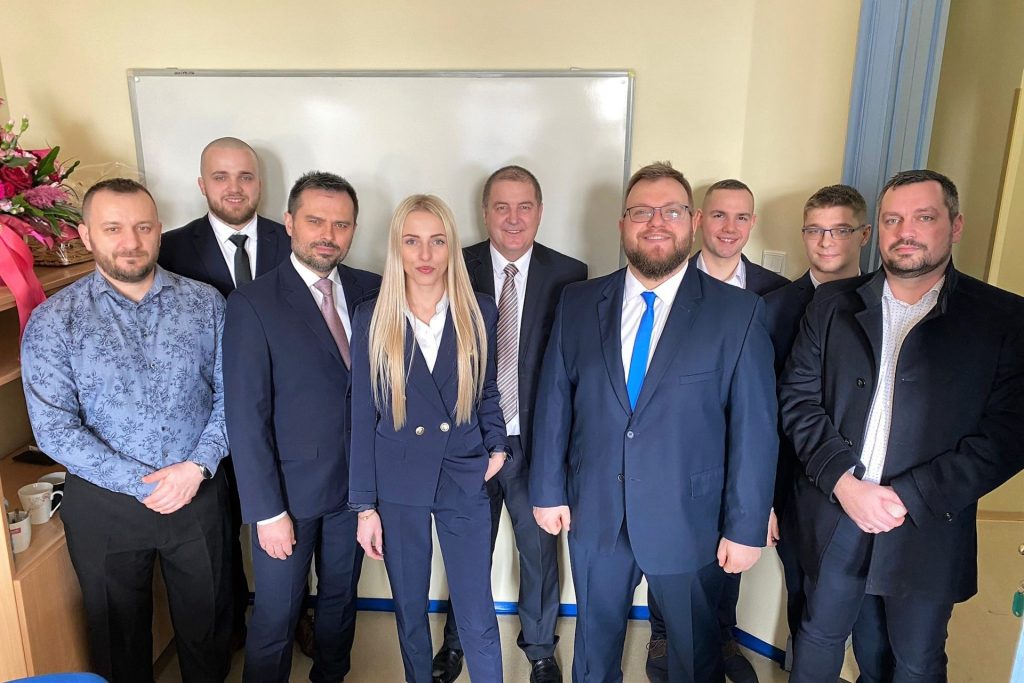 Grupa uczestników spotkania pozuje w sali przy tablicy.