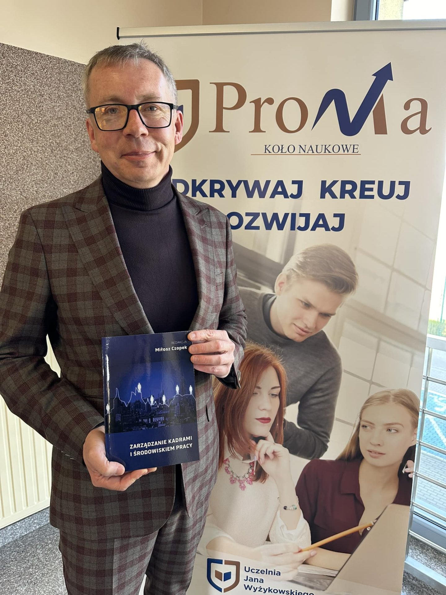 A smiling man is standing, holding a book in his hands