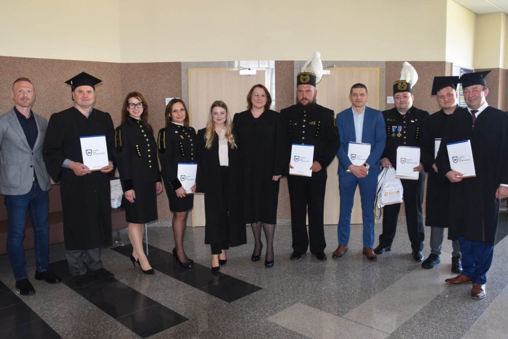 Absolwenci z dyplomami i uczestnicy uroczystości pozują w holu; część osób nosi mundury górnicze.