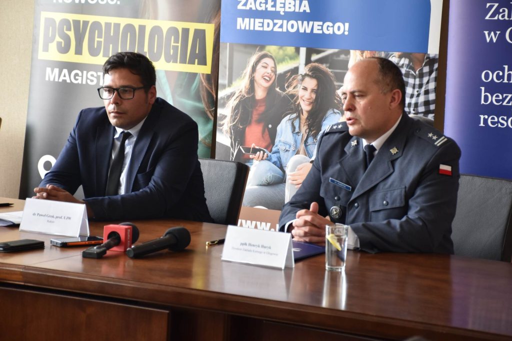 Dwóch mężczyzn siedzi przy stole prezydialnym. Jeden z nich przemawia.