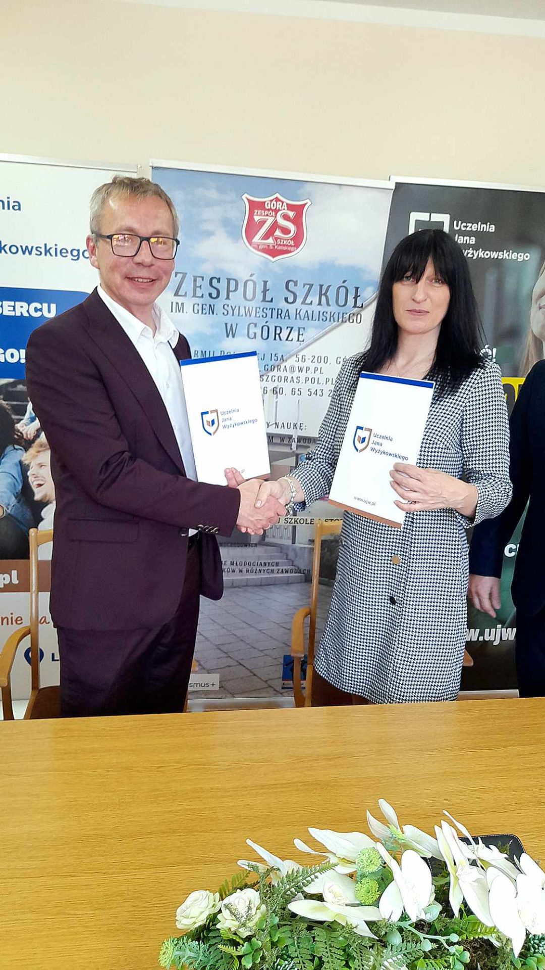 Kobieta i mężczyzna stoją uśmiechnięci przy stole i ściskają sobie dłonie