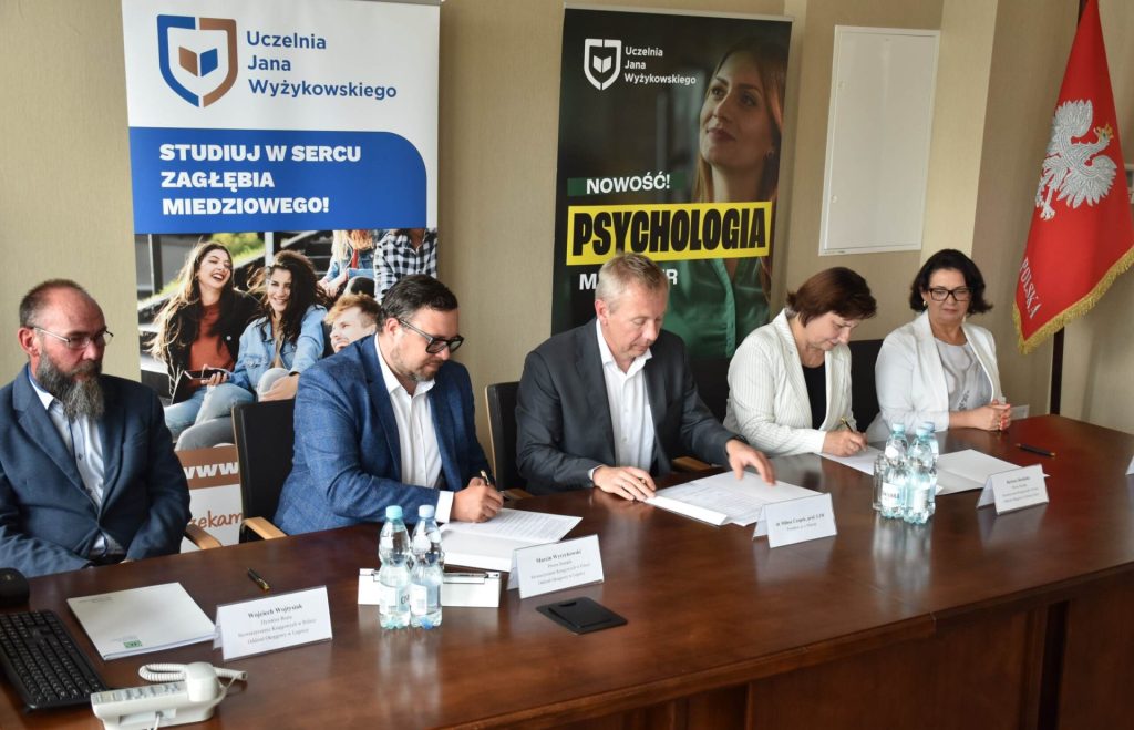 Przedstawiciele uczelni i partnera podpisują dokumenty przy stole konferencyjnym.