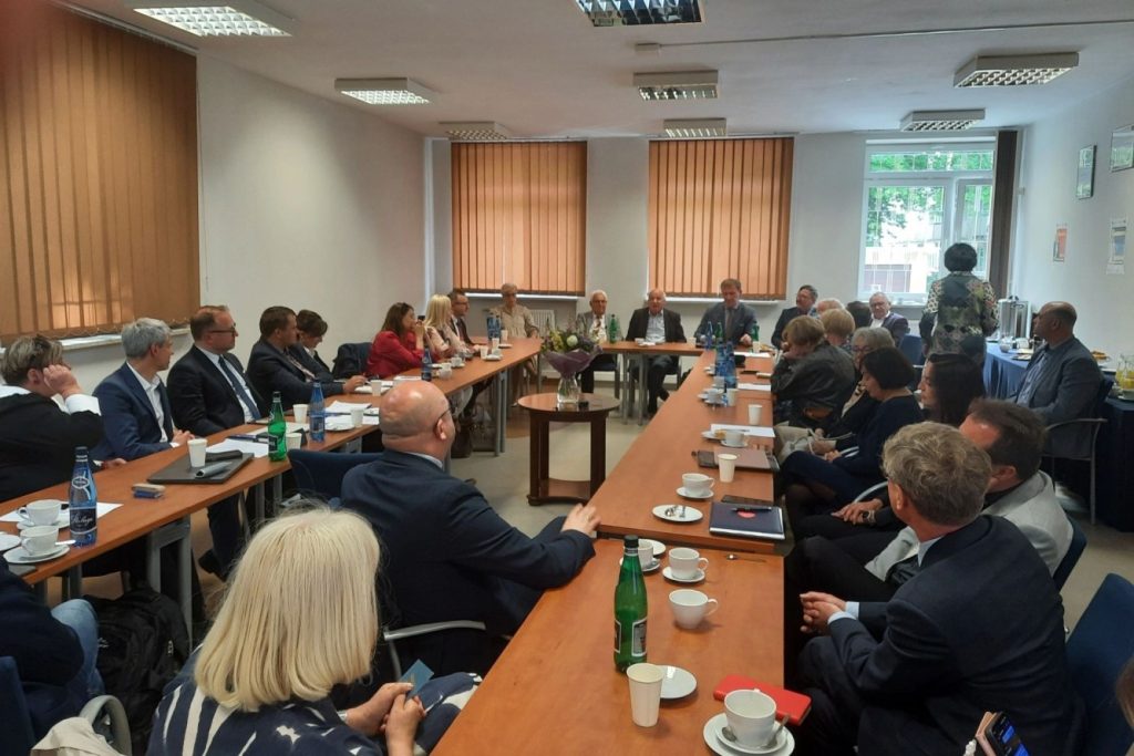 Uczestnicy obrad siedzą przy stołach ustawionych w podkowę.