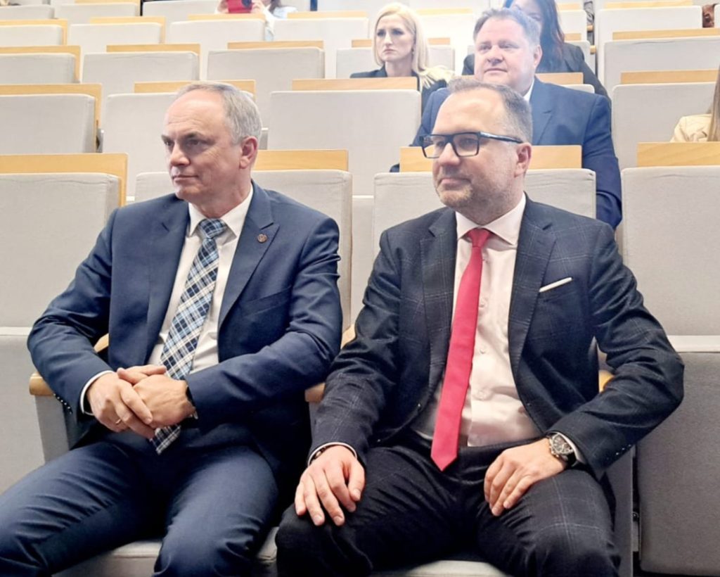 Dwaj mężczyźni w garniturach siedzą w pierwszym rzędzie podczas konferencji studenckiej.