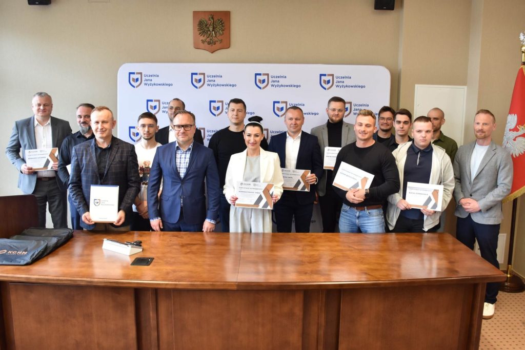 Grupa uczestników uroczystości prezentuje certyfikaty w sali UJW.
