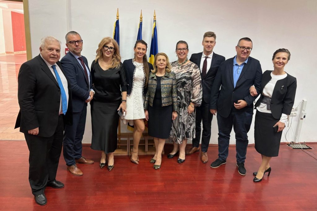 Uczestnicy oficjalnego spotkania pozują przy flagach w sali konferencyjnej.