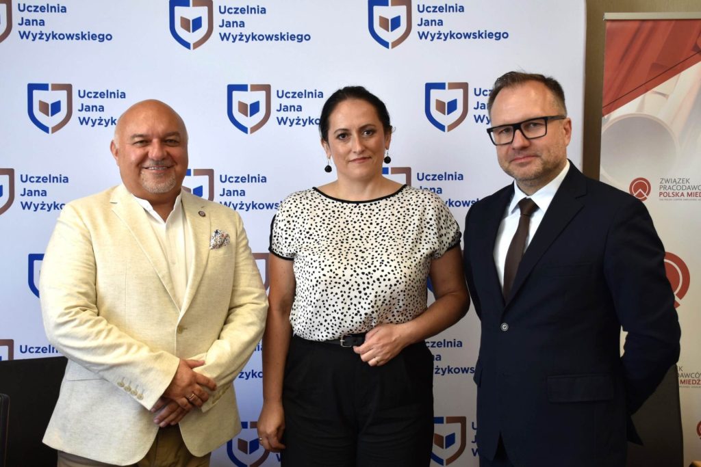 Kobieta i dwaj mężczyźni pozują na tle planszy UJW.