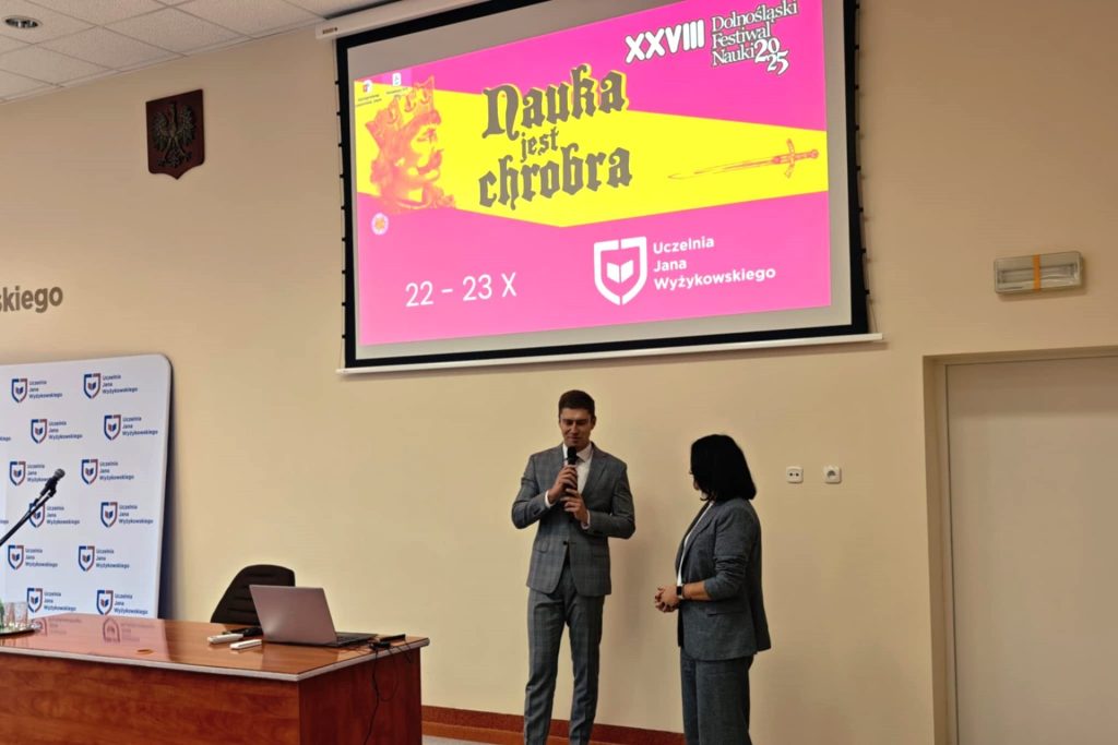 Dwie osoby z mikrofonami na scenie przy planszy Dolnośląskiego Festiwalu Nauki.