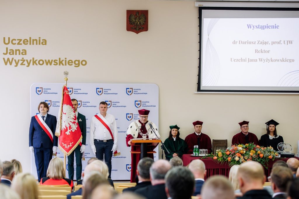inauguracja nowego roku akademickiego. Na zdjęciu są władze uczelni, sztandar UJW, zaproszeni goście, w tle wyświetla sie napis - wystapienie rektora UJW dra Dariusza Zająca