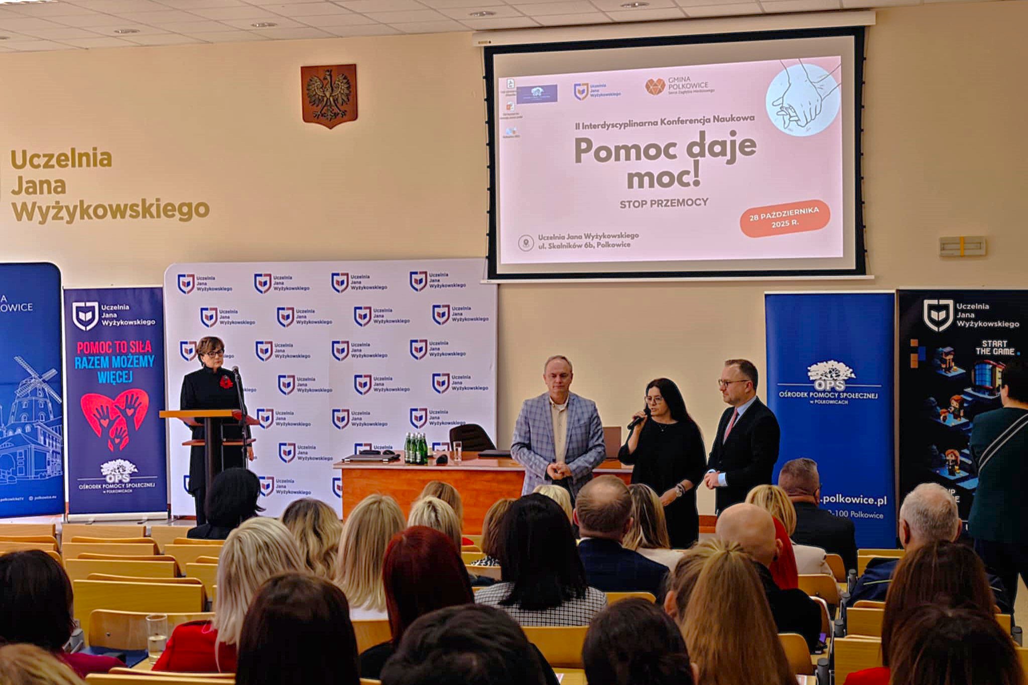 na zdjęciu widac Pana Burmistrza, Pana Rektora oraz Panią Dyrektor OPS. obok Pani dr Joanna Mesjasz. w tle różówy plakat Pomoc daje moc