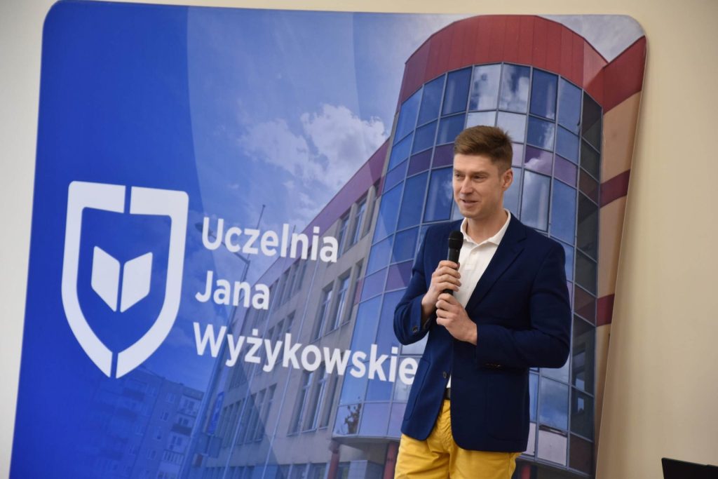 Prelegent z mikrofonem przed ścianką UJW podczas Dnia Drzwi Otwartych.