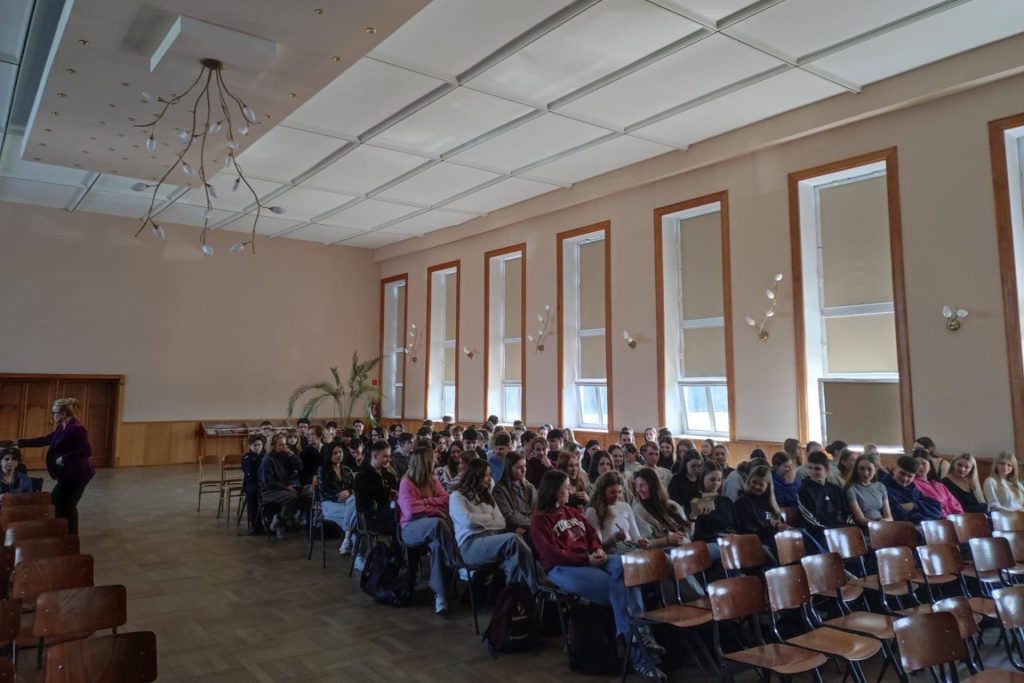 Uczniowie słuchają wystąpienia w dużej sali szkolnej.