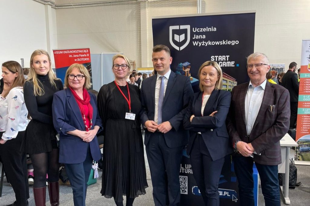 Grupa gości targów edukacyjnych na tle roll-upu UJW.