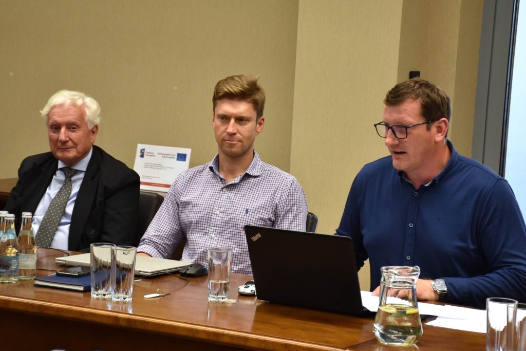 Trzej uczestnicy posiedzenia Senatu UJW siedzą przy stole; jeden korzysta z laptopa.