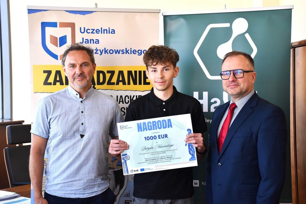 Laureat prezentuje nagrodę o wartości 1000 EUR, stojąc między dwoma przedstawicielami uczelni.