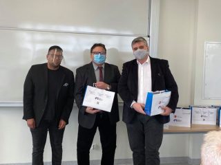 Trzej mężczyźni pozują do zdjęcia z dyplomami i nagrodami.