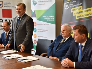 Mężczyzna w szarym garniturze zabiera głos przy stole z przedstawicielami partnerów UJW.