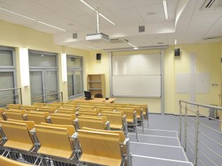 Sala wykładowa ze schodkową widownią, projektorem i białą tablicą.