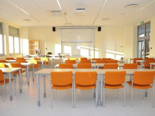 Jasna sala ćwiczeniowa UJW z pomarańczowymi krzesłami i ekranem projekcyjnym.