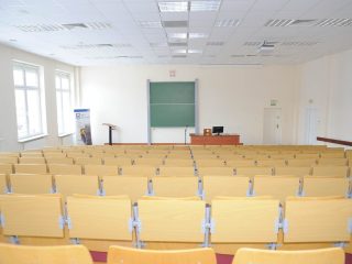 Duża aula z rzędami drewnianych pulpitów i zieloną tablicą.