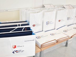 Torby upominkowe i teczki z dyplomami rozłożone przy ścianie sali.