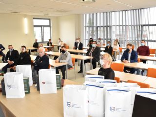 Uczestnicy uroczystości nagród siedzą przy oddzielnych stolikach; na pierwszym planie torby z logo UJW.