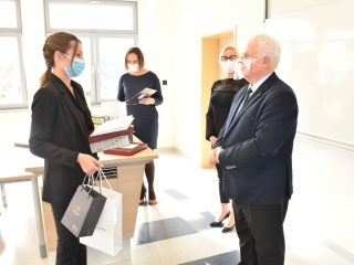 Kobieta w czarnej marynarce trzyma książki i torbę upominkową podczas rozmowy z wręczającym nagrody.
