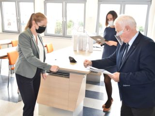 Kobieta w szarej marynarce i siwowłosy mężczyzna wyciągają pięści do powitania podczas wręczania nagród.