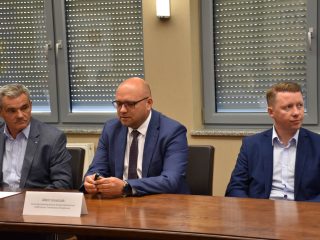 Trzej uczestnicy spotkania klastra energetycznego przy stole z wizytówkami.