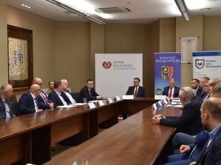 Obrady klastra energetycznego przy stołach ustawionych w podkowę.