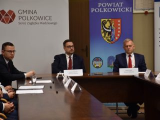 Uczestnicy spotkania siedzą pod banerami Gminy Polkowice i Powiatu Polkowickiego.