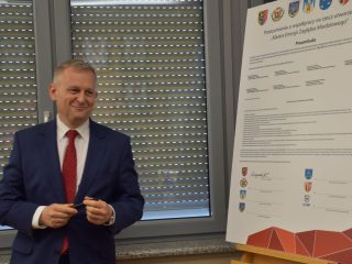 Mężczyzna w granatowym garniturze i czerwonym krawacie stoi obok dokumentu klastra.