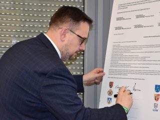Przedstawiciel w okularach składa podpis na planszy porozumienia.