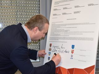 Uczestnik w granatowej marynarce pochyla się nad planszą, składając podpis.