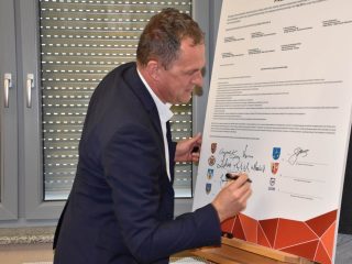 Uczestnik spotkania podpisuje dokument na sztaludze przy oknie.