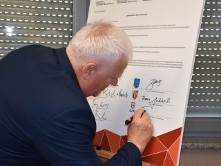 Siwowłosy mężczyzna podpisuje duży dokument porozumienia klastra energetycznego.