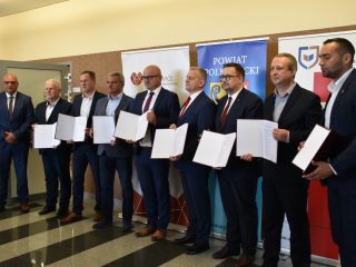 Sygnatariusze porozumienia pozują z otwartymi teczkami i dokumentami.