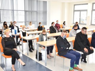 Uczestnicy wręczenia nagród siedzą w sali przy stolikach i na krzesłach.