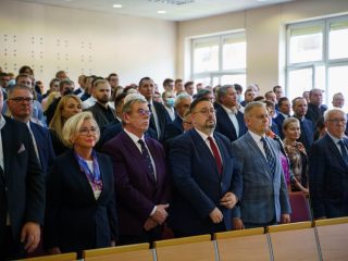 Uczestnicy inauguracji stoją w rzędach w auli.