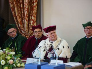 Czterej przedstawiciele uczelni w uroczystych togach siedzą przy stole podczas inauguracji.